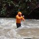 person in stream with brown water holding an instrument in the water. 